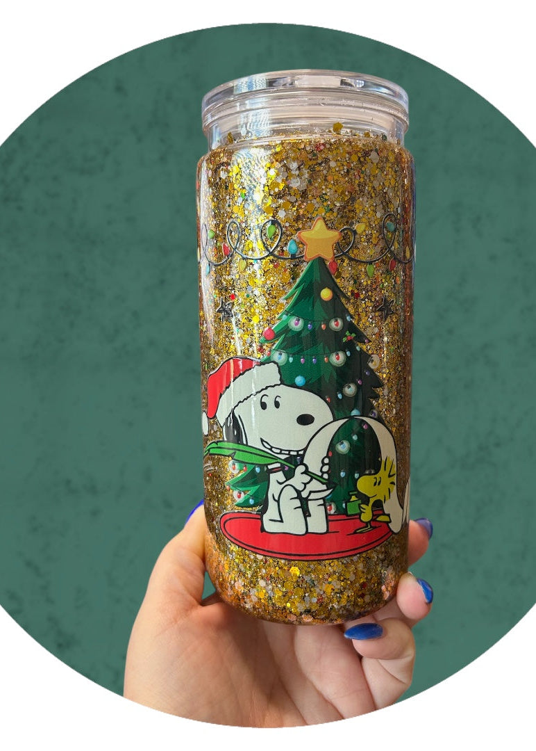 Tumbler with Snoopy and Christmas tree design held by a hand against a green background