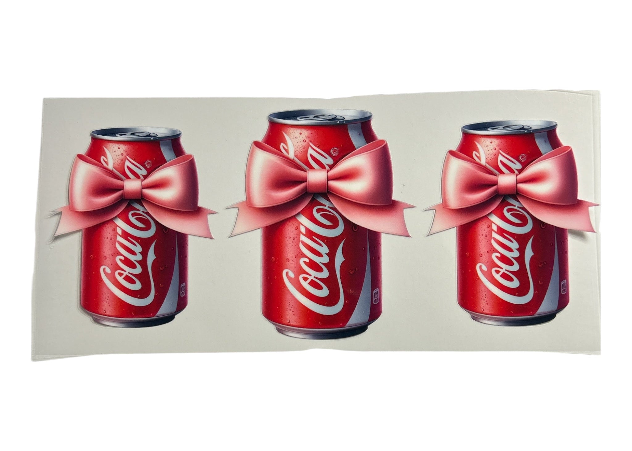 Three Coca-Cola cans with pink bows on a white background