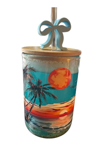 Close-up of 16oz beach-themed double wall glass tumbler with palm tree wrap, triple-washed sand and shimmering ocean liquid