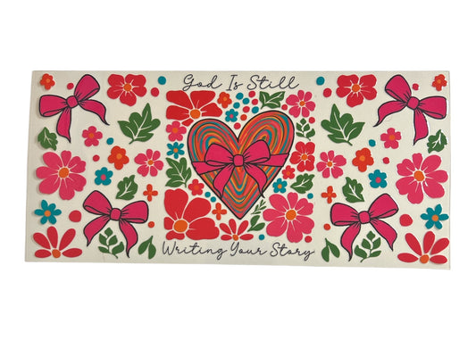 Decorative cup wrap with heart, flowers, and 'God Is Still Writing Your Story' text on a clear background