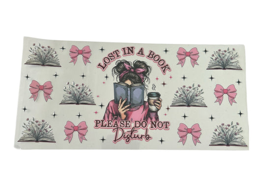 Decorative cup wrap with a person reading a book and text 'Lost in a Book, Please Do Not Disturb' on a clear background.